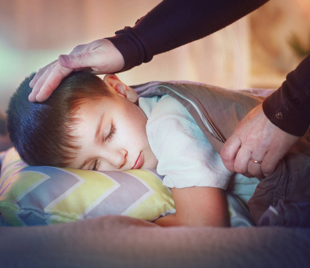 Pieni poika nukkuu ja haaveilee sängyssä, äiti peittää pojan peitolla
 - Valokuva, kuva