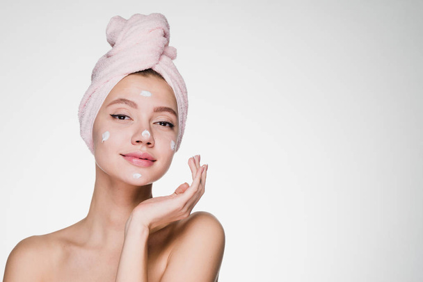 cute attractive girl with pink towel on her head applying white moisturizer on face - Фото, изображение