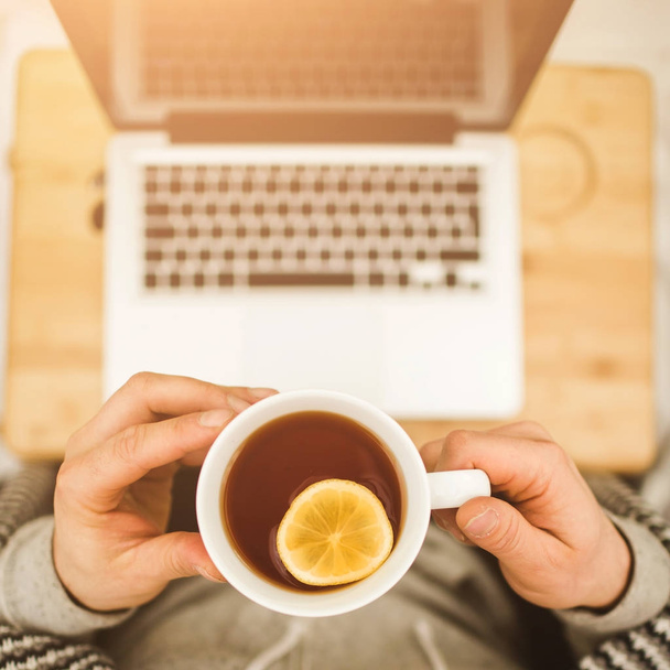 Top view hands with cup of tea with lemon and laptop - Foto, Imagen