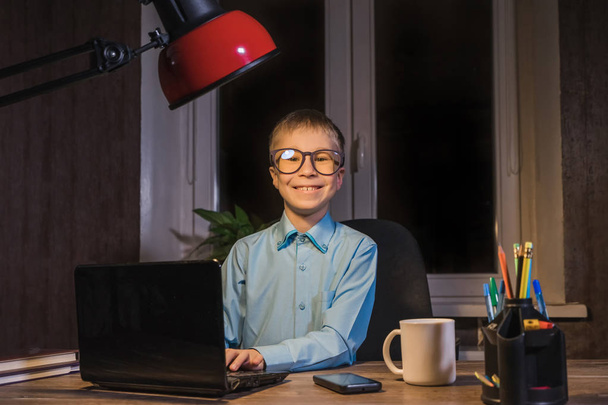 Criança feliz em óculos sentada à mesa e mensagens de texto no laptop
.  - Foto, Imagem