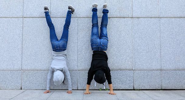Two female hipsters doing handstand against wall in city - Foto, Bild