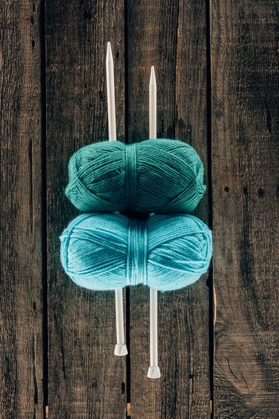 top view of blue and green yarn with knitting needles on wooden background - Foto, Bild