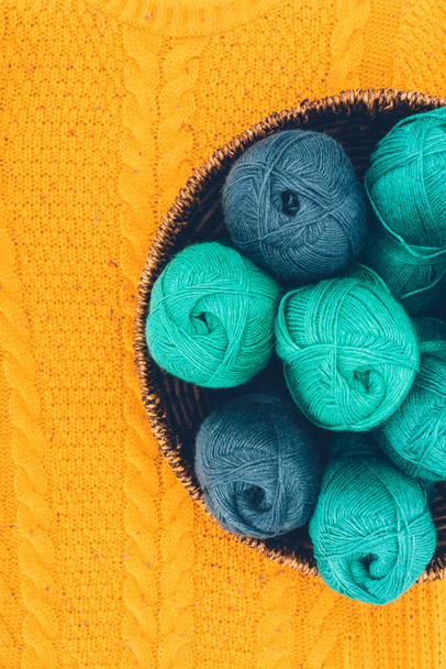 bovenaanzicht van blauw en groen garen ballen in rieten mand op gele tricot breien - Foto, afbeelding