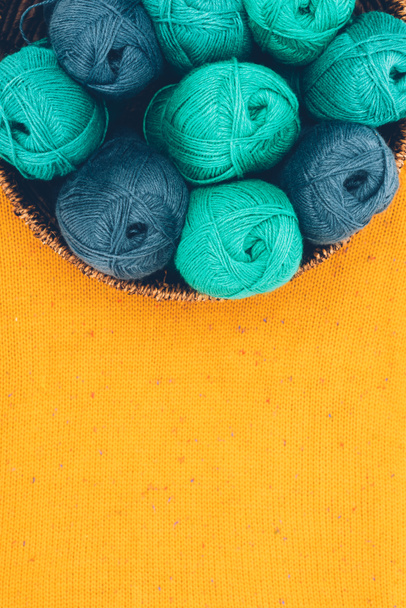vue de dessus des boules de laine tricotées bleues et vertes dans un panier en osier sur maille jaune
 - Photo, image