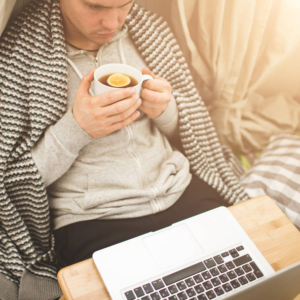 Młody człowiek w bad z laptopa i filiżankę herbaty. - Zdjęcie, obraz