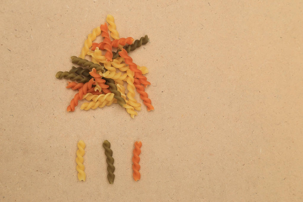 rohe dreifarbige Spirale Twist Pasta auf braunen Sperrholzhintergründen als Wolken und Regen mit Platz für Text. - Foto, Bild