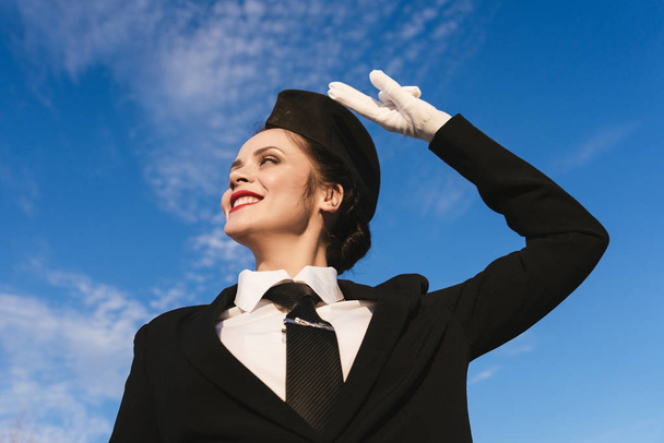 beautiful young woman stewardess in uniform shows two fingers under blue sky - Foto, imagen