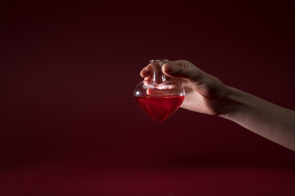 cropped image of woman holding heart shaped glass jar of perfume isolated on red - Foto, Bild