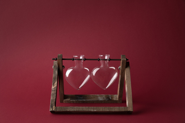 two empty heart shaped glass jars on wooden stand on red - Photo, Image
