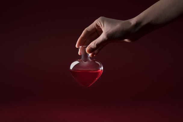 bijgesneden afbeelding van vrouw met hartvormige glazen pot van liefdeselixer geïsoleerd op rood - Foto, afbeelding