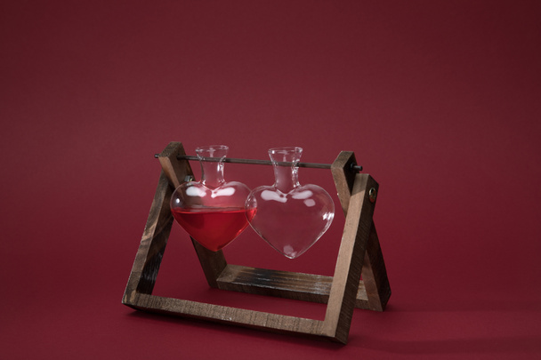 heart shaped glass jar with perfume and empty glass jar on wooden stand on red - Foto, Bild