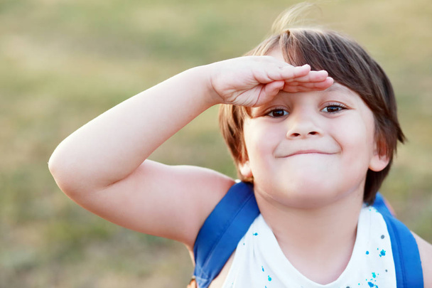 smiling little boy salutes or covering his face from sun with his hand - Photo, Image