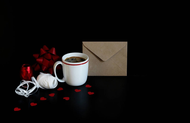 Valentines day or wedding still life scene with cup of coffee, envelope, paper hearts confetti and decorative gift ribbons over black background. Love concept. Front view. Empty space for your text. - Foto, Imagen