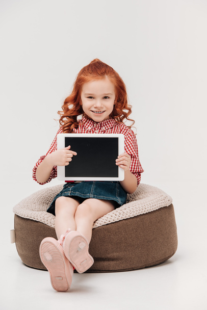adorable redhead child smiling at camera and pointing at digital tablet with blank screen isolated on grey - Foto, Imagen