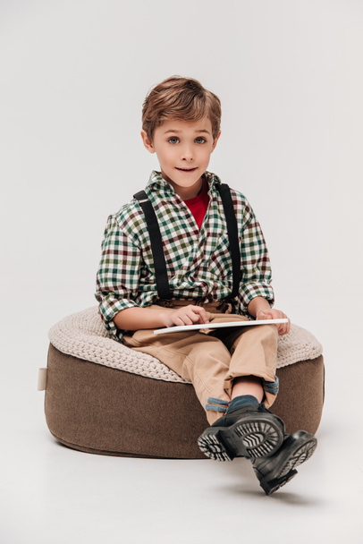 schattige kleine jongen met behulp van digitale tablet en lachend op camera geïsoleerd op grijs - Foto, afbeelding