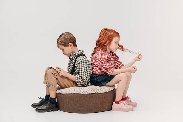 children sitting back to back while boy using digital tablet isolated on grey - Photo, Image