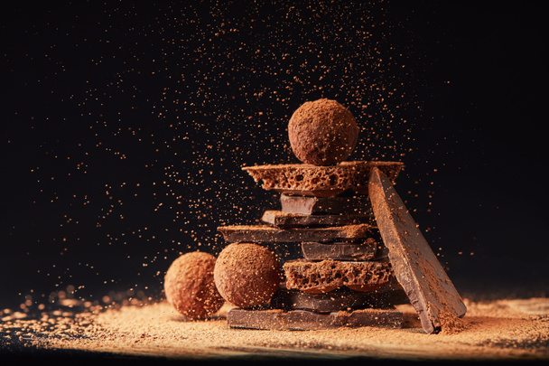 close up view of arrangement of truffles and chocolate bars with cocoa powder on black - Фото, зображення