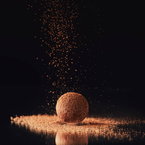close up view of sweet truffle candy with cocoa powder on black - Foto, afbeelding