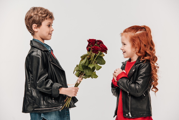 グレーに分離された彼のガール フレンドにバラの花束を提示の小さな男の子の側面図 - 写真・画像