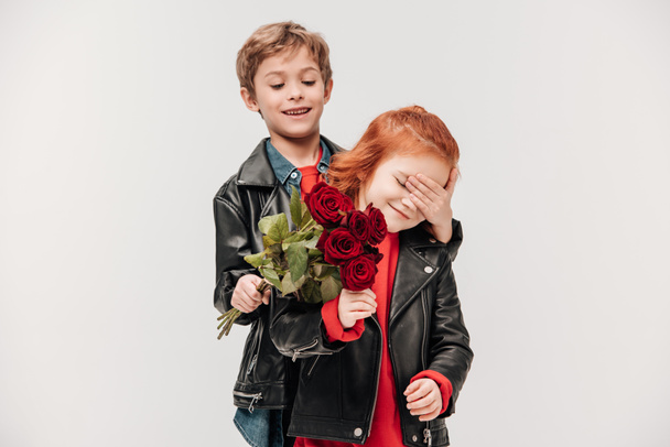 glücklicher Junge überreicht Rosenstrauß an seine kleine Freundin isoliert auf grau - Foto, Bild
