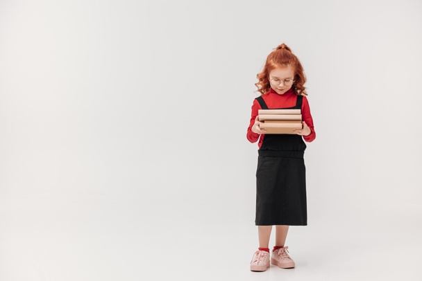 beautiful little schoolgirl carrying stack of books isolated on grey - Foto, afbeelding