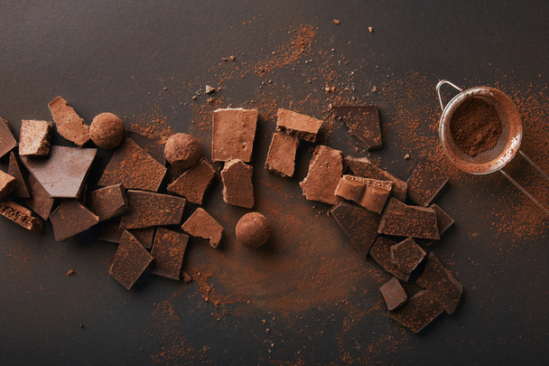 top view of arrangement of various types of chocolate, truffles and sieve with cocoa powder - Foto, immagini