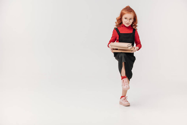 прелестная маленькая школьница с стопкой книг, изолированных на сером
 - Фото, изображение
