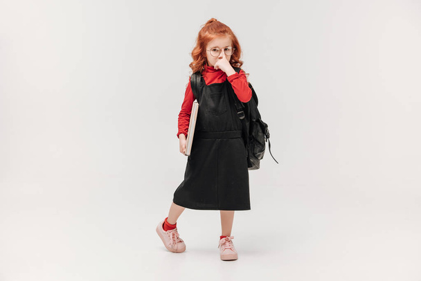 serious  little schoolgirl in black dress with big book isolated on grey - Foto, Imagen