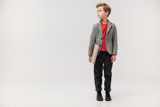 stylish little schoolboy with big book isolated on grey - Foto, imagen