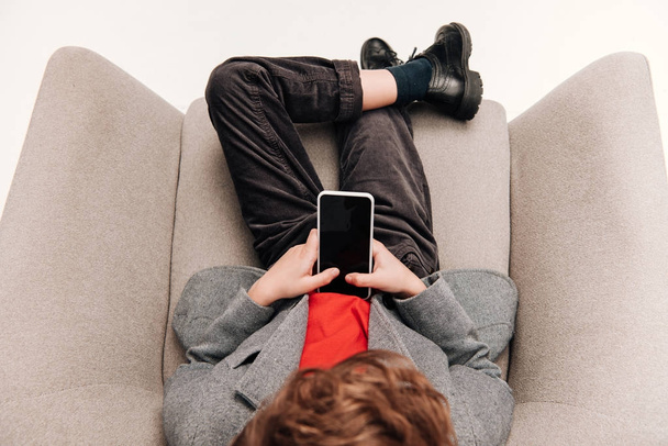 top view of stylish little boy using smartphone in armchair - Фото, изображение