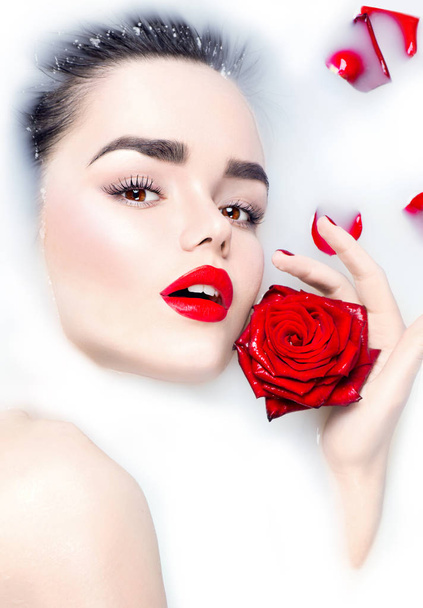  young model with red lips and red rose flower in milk bath - Φωτογραφία, εικόνα