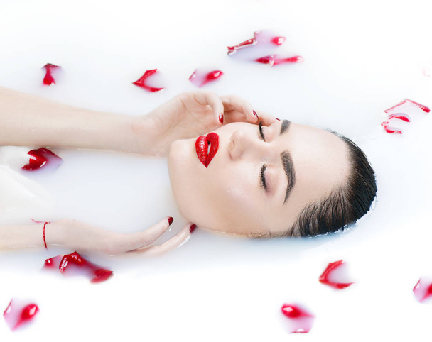 Woman portrait with red rose petals in milk bath - Foto, imagen