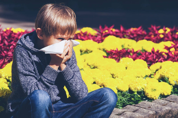 Child having allergy. Boy sitting outdoor with tissue in city park - Photo, Image