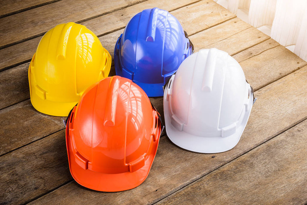 biały, niebieski, pomarańczowy, żółty twardego bezpieczeństwa hełm kapelusz budowy dla bezpieczeństwa projektu robotnika jako inżynier lub pracownika, Budownictwo inżynieryjne robotnik sprzęt, na drewnianej podłodze - Zdjęcie, obraz