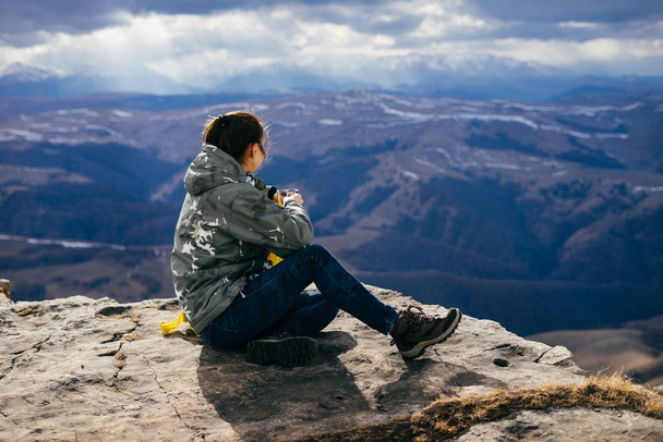 giovane ragazza si siede sul bordo della scogliera, gode le montagne del Caucaso e il sole
 - Foto, immagini