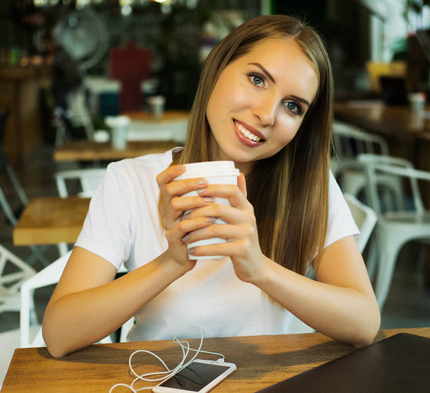 Hymyilevä nainen hyvällä tuulella kupin kahvia istuu kahvilassa. - Valokuva, kuva