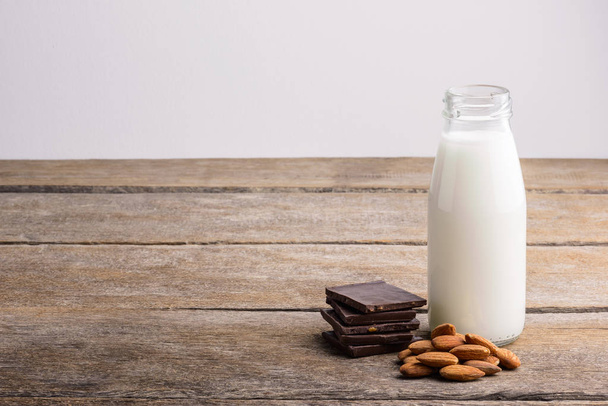 melk in fles, chocolade en amandel op houten achtergrond - Foto, afbeelding