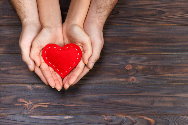Amor, concepto familiar. Primer plano de las manos de hombre y mujer que sostienen el corazón de goma roja juntos
 - Foto, Imagen