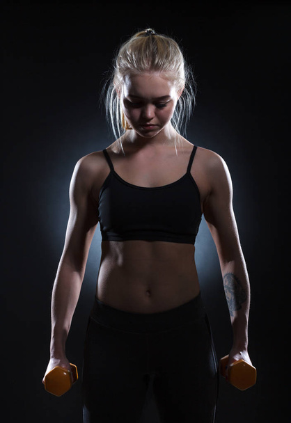 Young woman with dumbbells on a dark background. - Photo, image