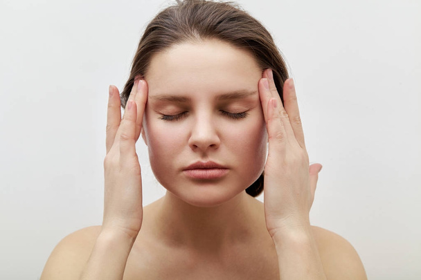 young female model with closed eyes making herself facial massage while softly touching skin and applying gentle pressure, daily beauty routine concept - Zdjęcie, obraz