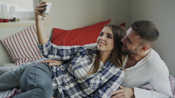Married happy couple taking selfie portrain while lying on bed at home in the morning - Foto, afbeelding