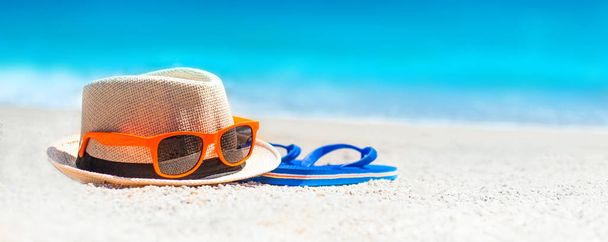 Flip flops, beach hat, sun glasses on the sand. Summer vacation concept. Sunny day on tropical beach with blue sea horizon - Foto, immagini