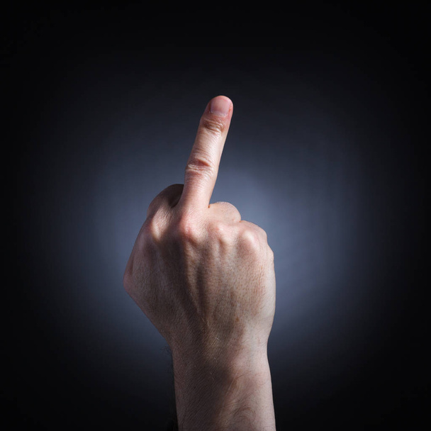 Человеческая рука в непристойном жесте с поднятым средним пальцем крупным планом на темном фоне
. - Фото, изображение