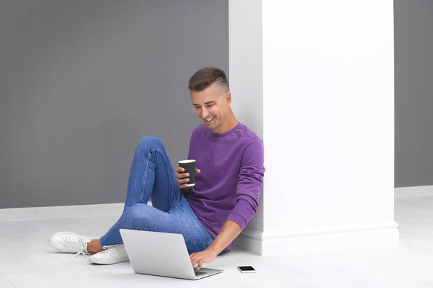 Young man using laptop and drinking coffee in light room - Foto, immagini