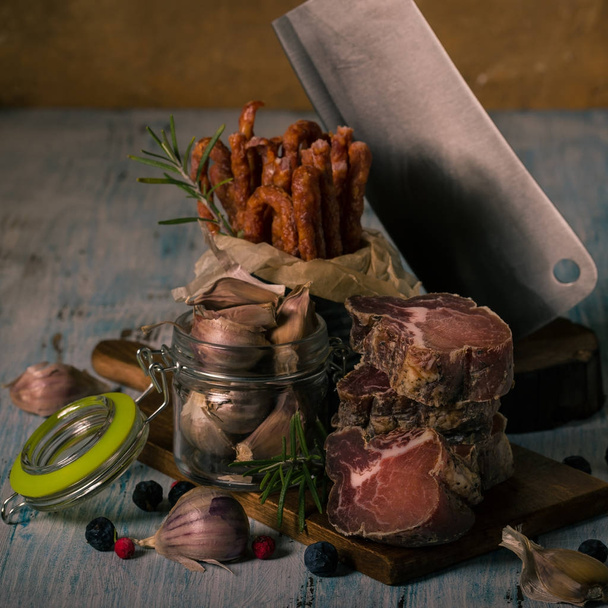 Dried italian meat from wild boar on cutting board with small sausages and garlic - Photo, Image