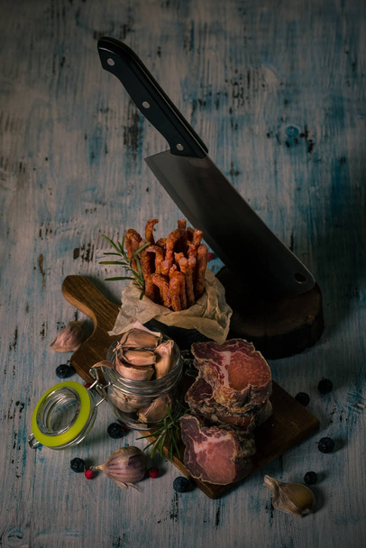 Dried meat from italian wild boar on cutting board with spiced sausages and garlic - Фото, изображение