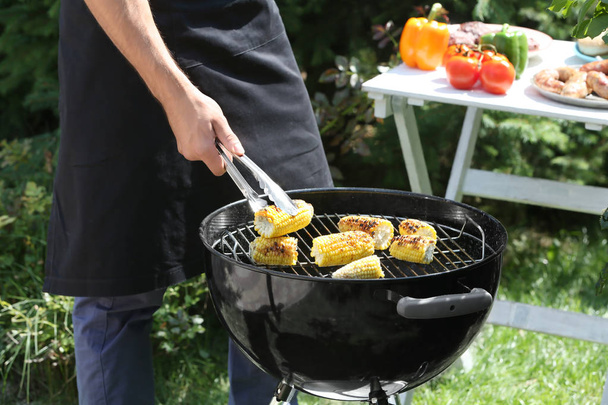 Man preparing delicious corn on barbecue grill outdoors - Foto, imagen