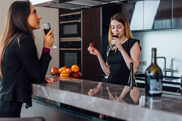 zwei beste Freundinnen feiern eine kleine Hausaufwärmparty, indem sie Rotwein trinken, der in der Küche steht - Foto, Bild
