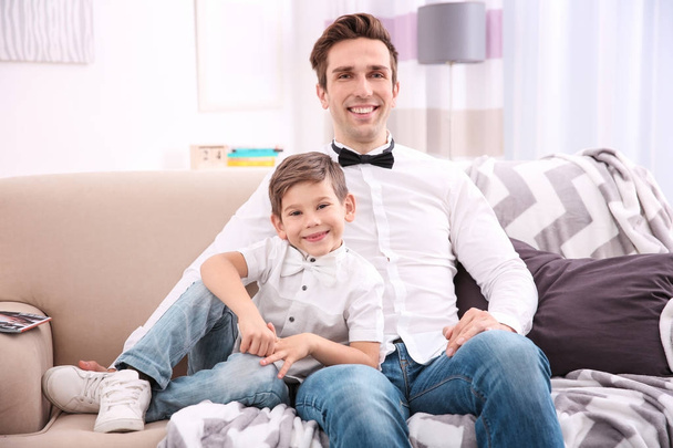 Father and son in shirts with bowties sitting on sofa at home - Фото, зображення