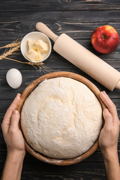 Woman holding bowl with fresh raw dough on wooden table - Foto, afbeelding